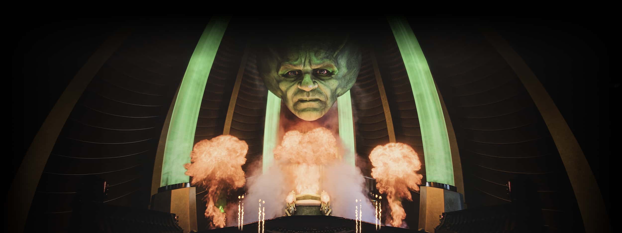 Wizard of Oz scene with a giant green floating head surrounded by smoke and fire inside a dark, glowing chamber